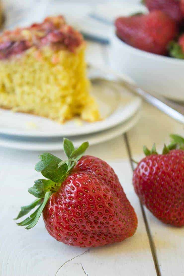 Two fresh strawberries in front of a slice of cake.