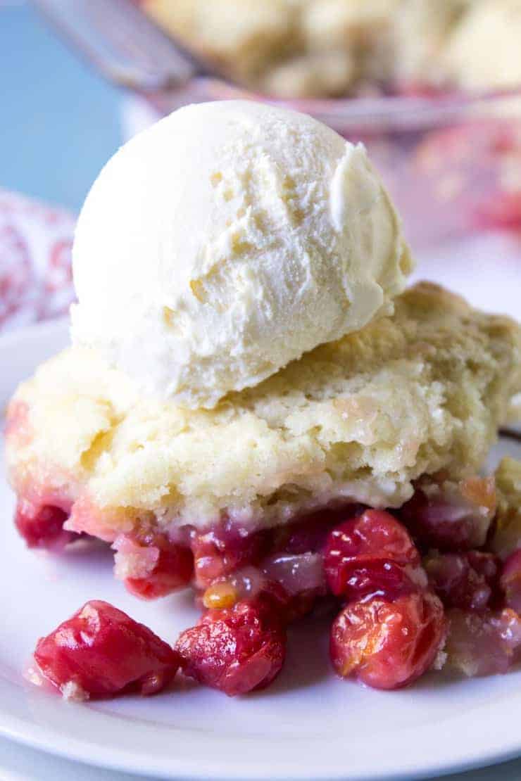 A scoop of ice cream on top of a sweet biscuit and cherries. 