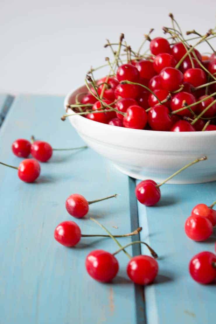 Fresh picked cherries in a white bowl and on a blue board.