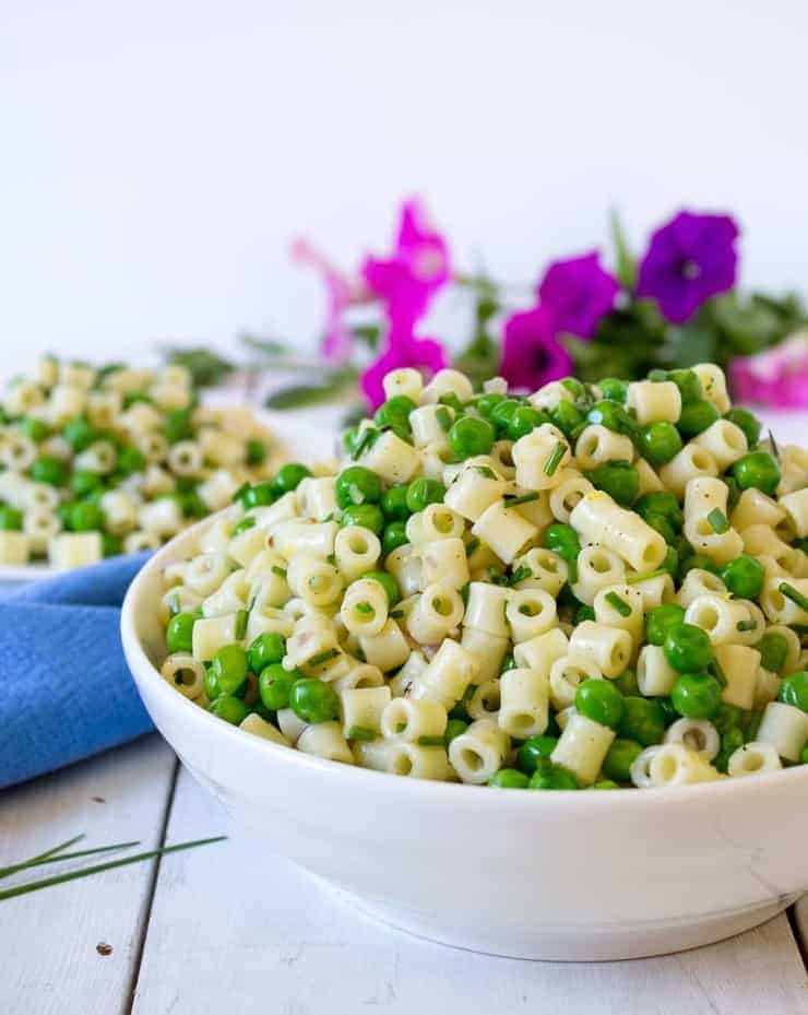 Large white bowl filled with small pasta and green peas.
