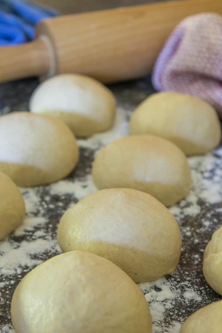 Balls of bread dough resting on a counter with flour on the counter. 