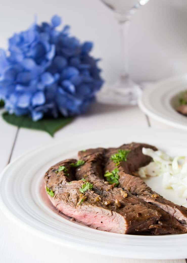 A plate with sliced steak topped with green parsley. 