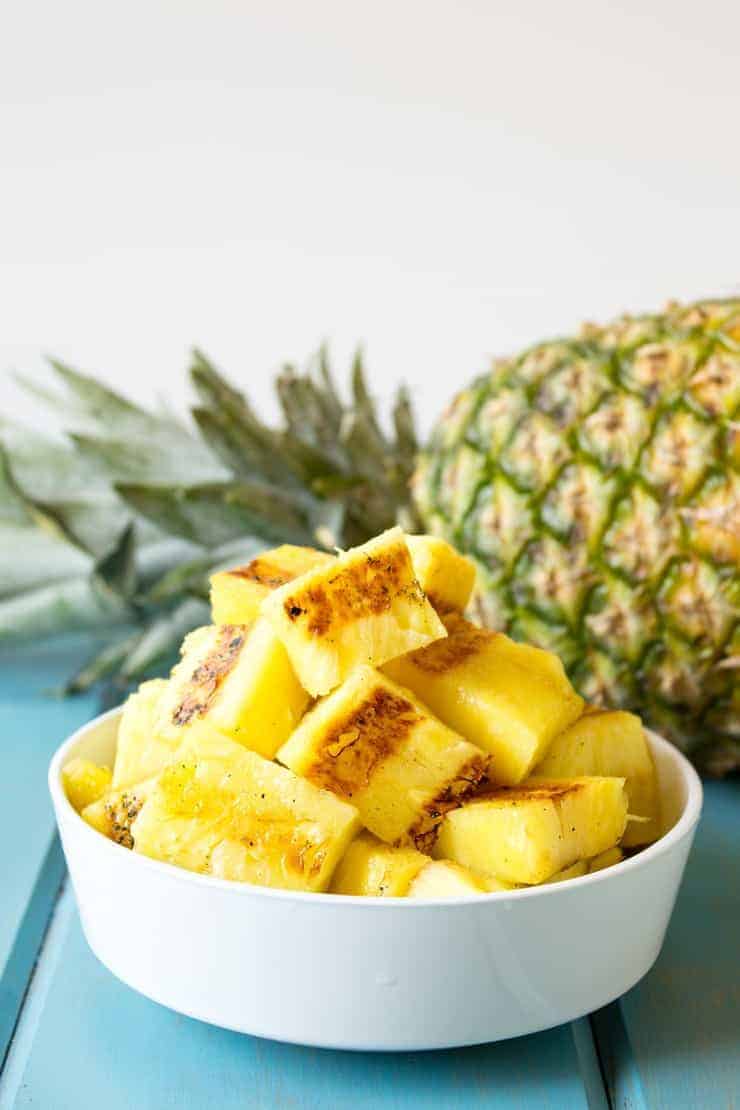 Grilled Pineapple in a white bowl with a whole pineapple in the background.