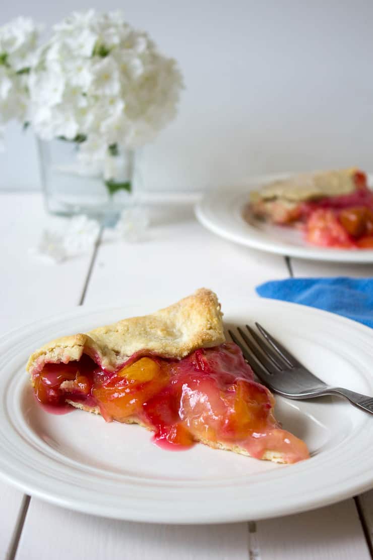 A slice of Plum Galette on a white plate with a fork next to the slice of pie. 