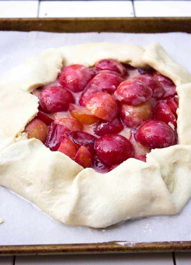 A pie crust filled with fresh plums on a baking sheet.