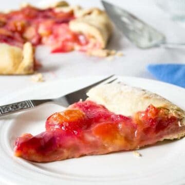 A slice of pie filled with plums resting on a white plate.