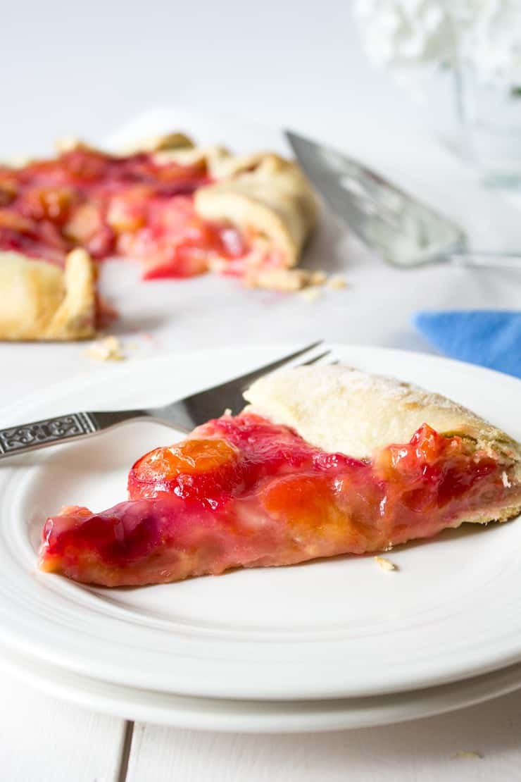 A slice of pie filled with plums on a white plate.
