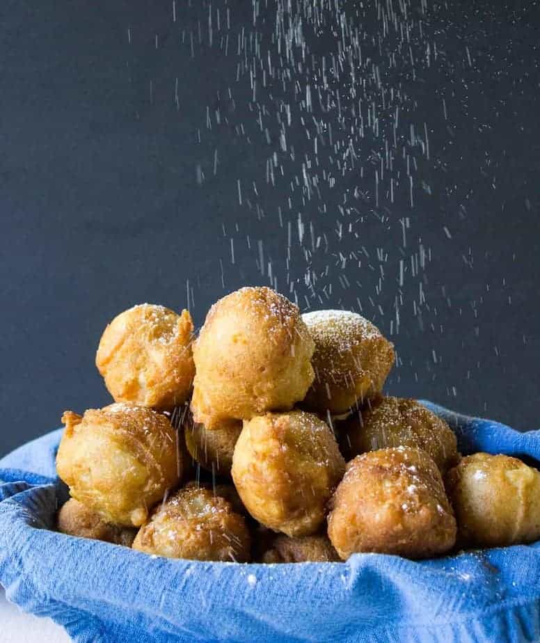 Powdered sugar sprinkling down on a basket of fried fritters.