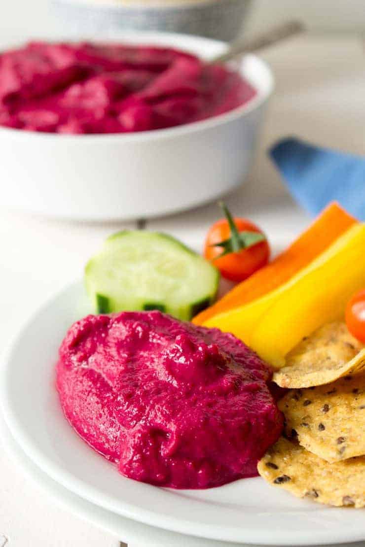 Beet hummus served on a white plate with chips and veggies.