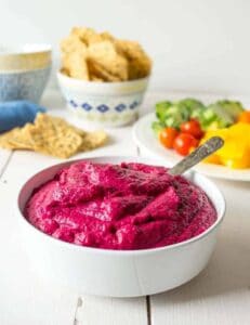 Bright pink hummus in a white bowl with a spoon.