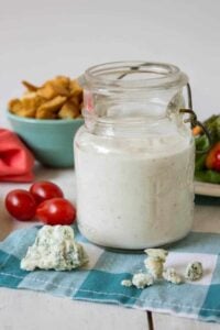 An old glass jar filled with a white salad dressing with crumbles of blue cheese in front of the jar.