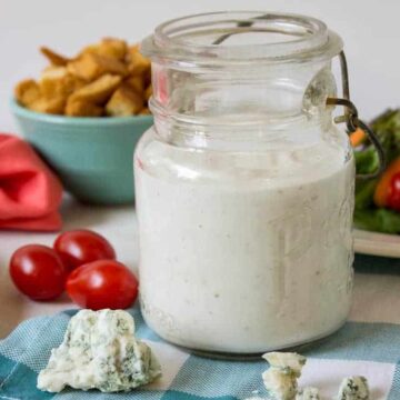 An old glass jar filled with a white salad dressing with crumbles of blue cheese in front of the jar.