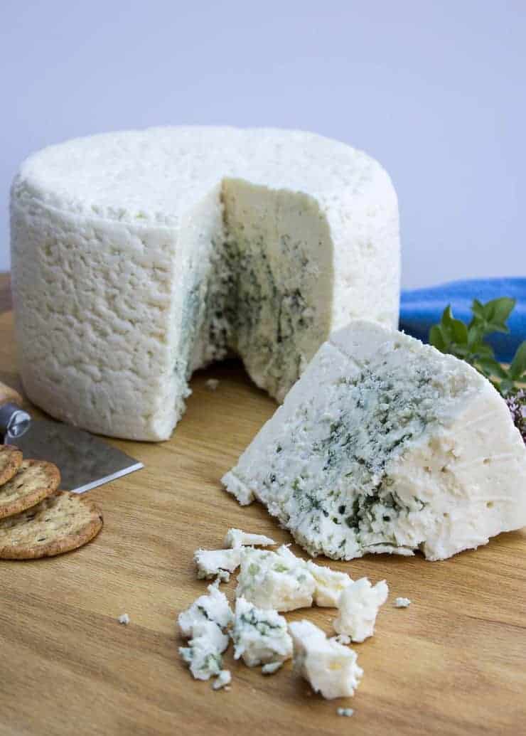 Wheel of blue cheese with a small wedge cut out of the wheel.