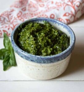 A small bowl filled with a dark green pesto with a basil leaf next to the bowl.