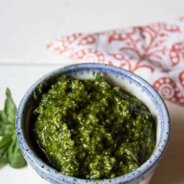 A small blue white bowl with a blue rim filled with a dark green pesto.