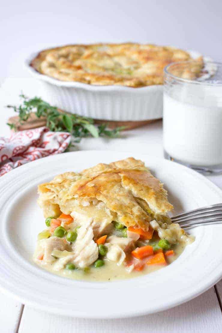 Chicken pot pie on a white dish with a glass of milk next to the dish.