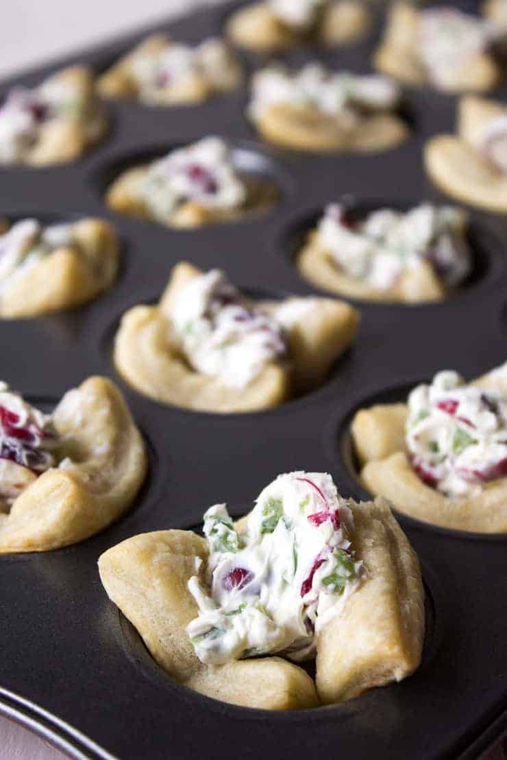 A mini muffin tin filled with puff pastry shells and a cream cheese mixture with cranberries and jalapenos.