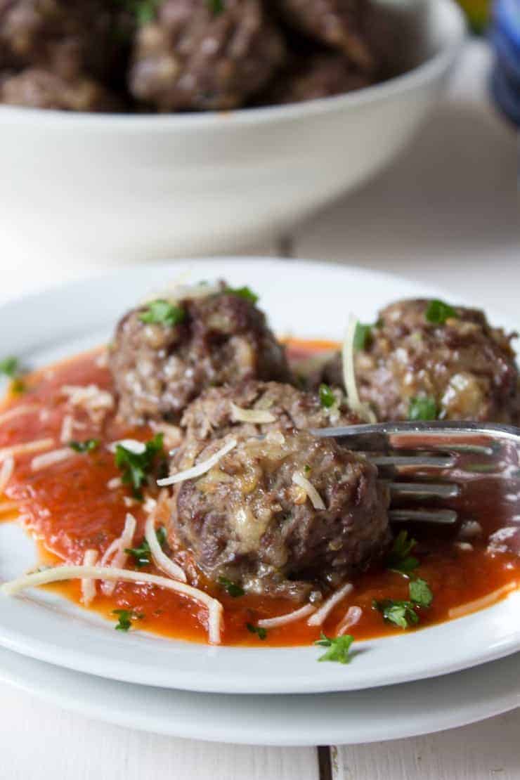 Three Italian meatballs on a small white plate with a fork.