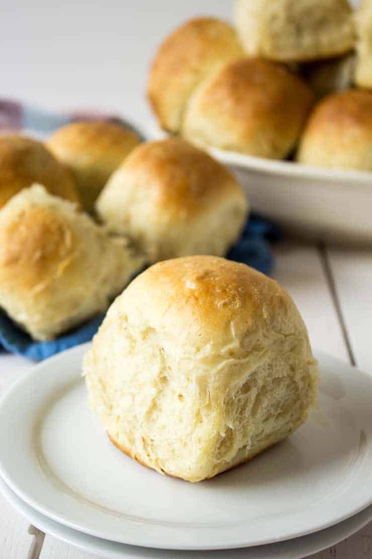 Homemade dinner rolls in a large bowl and a single roll on a small plate.