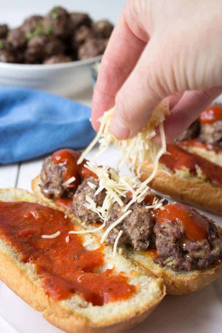 Meatball subs being topped with parmesan cheese.