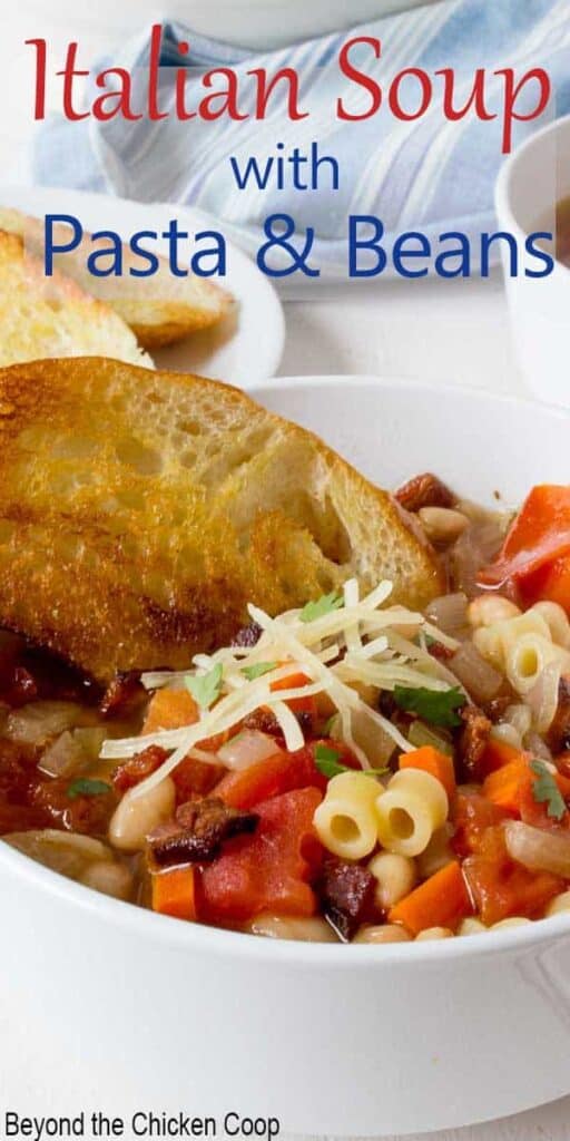 A bowl of soup filled with pasta, beans and vegetables served with a piece of toasted bread.