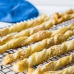 Puff pastry straws cooling on a rack. These straws are topped with sesame seeds.