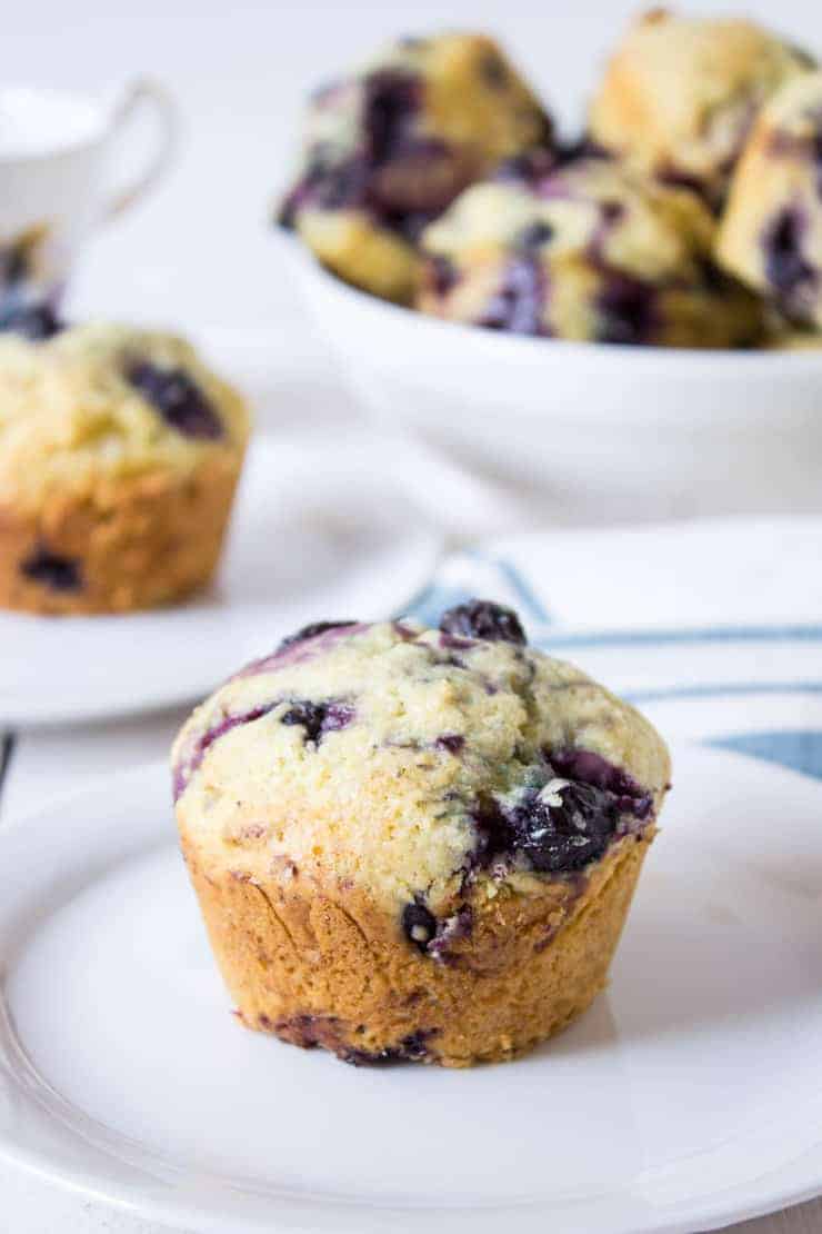 Muffins on a white plate with a bowl of muffins in the background.