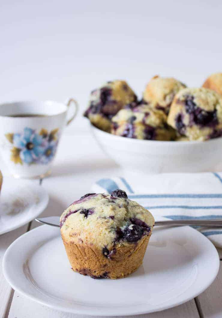 A muffin filled with fresh blueberries sitting on a white plate. 