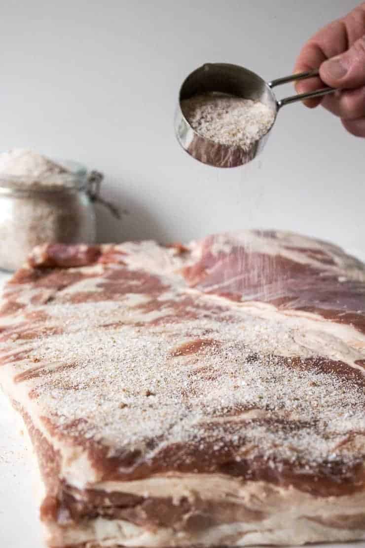 Pouring seasonings over a large slab of uncured bacon. 