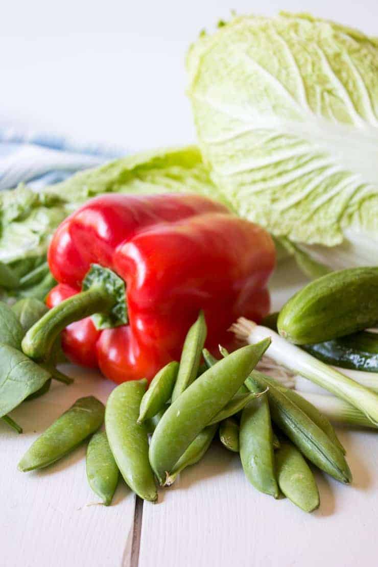 A red bell pepper, green peas, cabbage and onions on a board.