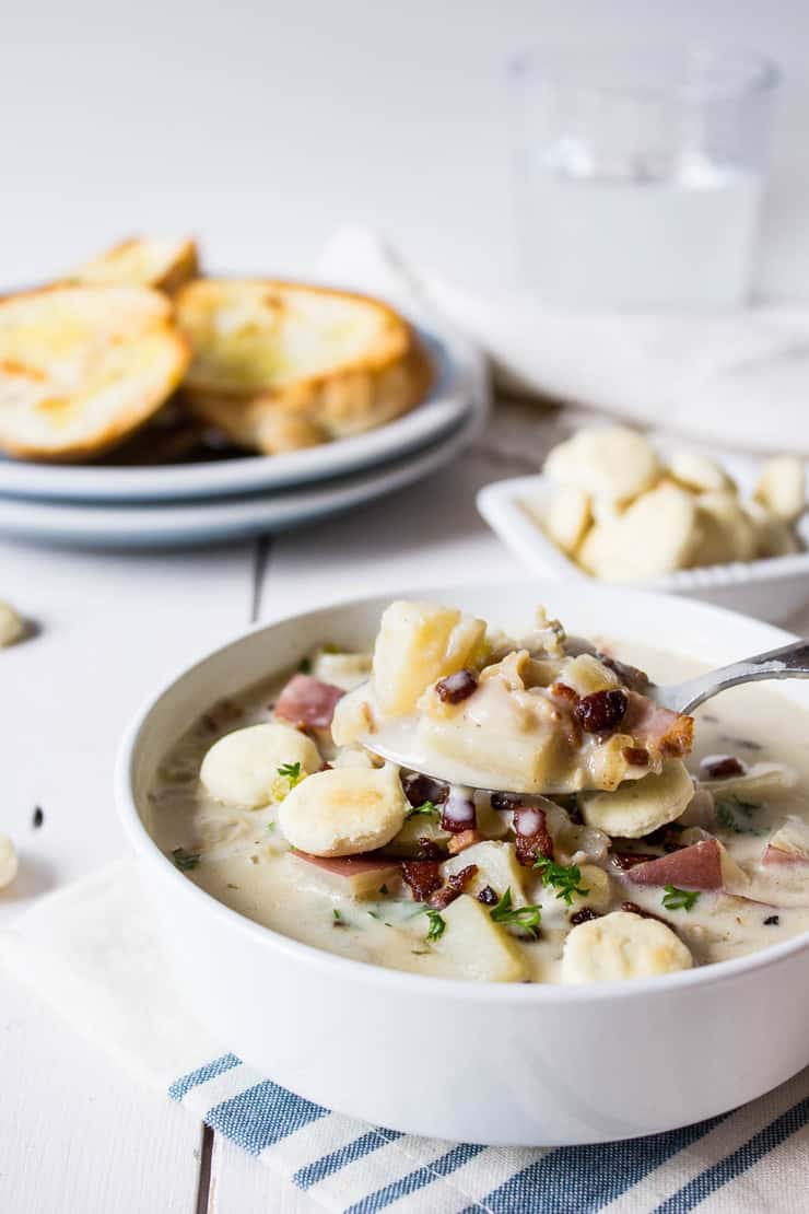 Spoonful of hot clam chowder topped with bacon and served in a white bowl. 