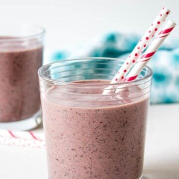 A red smoothie with two red and white straws in a glass.