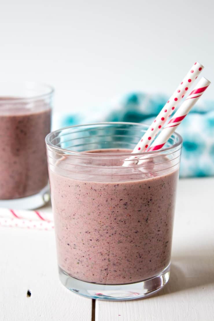 A glass filled with a red smoothie with two red and white straws in the glass.