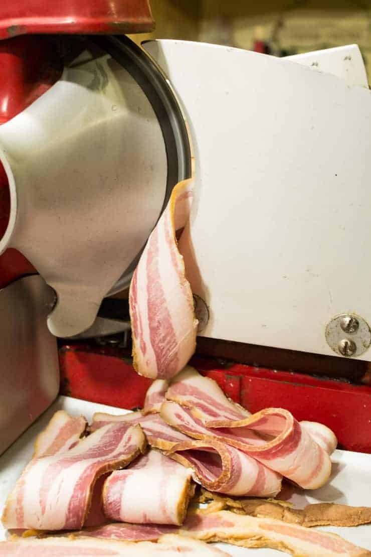 An old red meat slicer slicing bacon. 