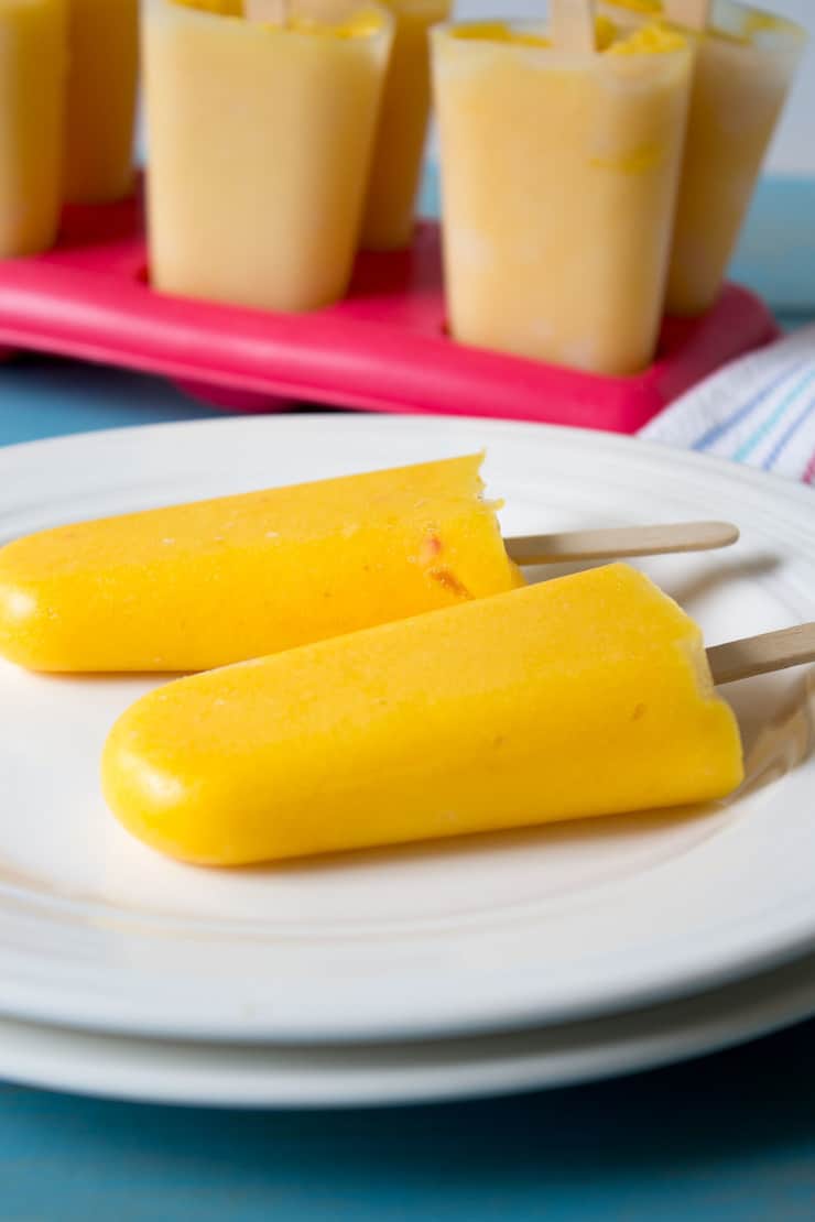 Yellow popsicles laying on a white plate. 