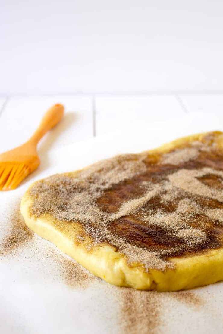 Bread dough in a rectangular shape covered with butter and cinnamon and sugar.