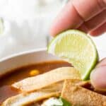 A lime wedge being squeezed over a bowl of soup.