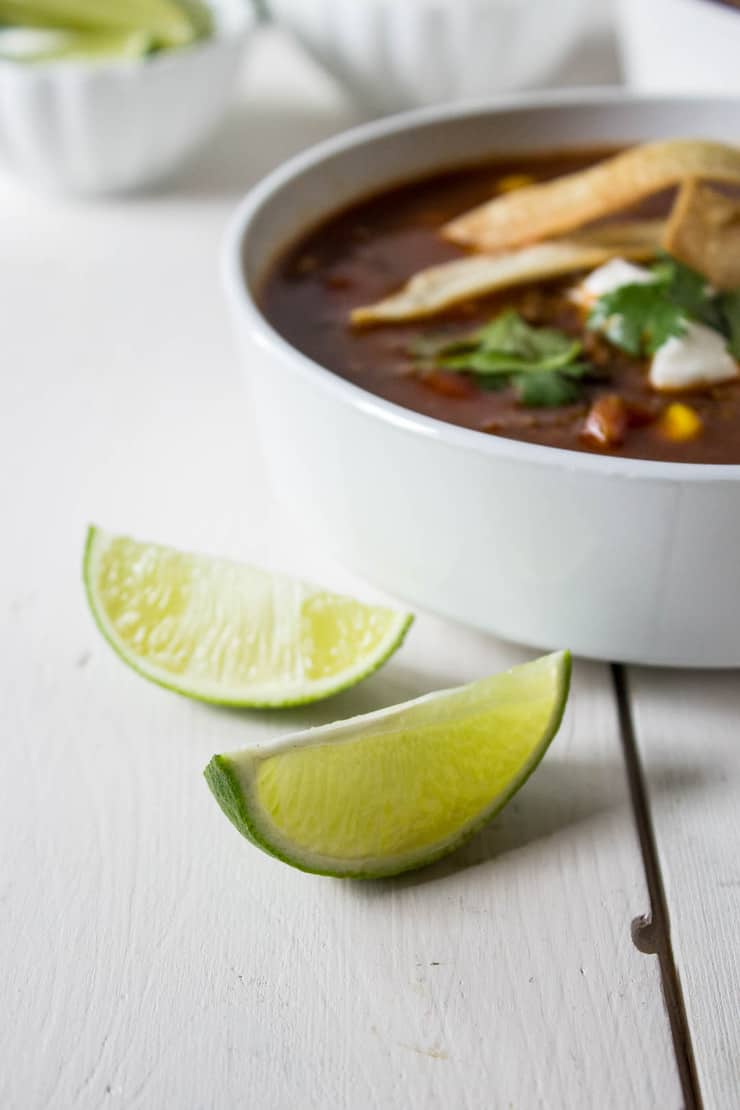 Sliced limes next to a bowl of soup. 