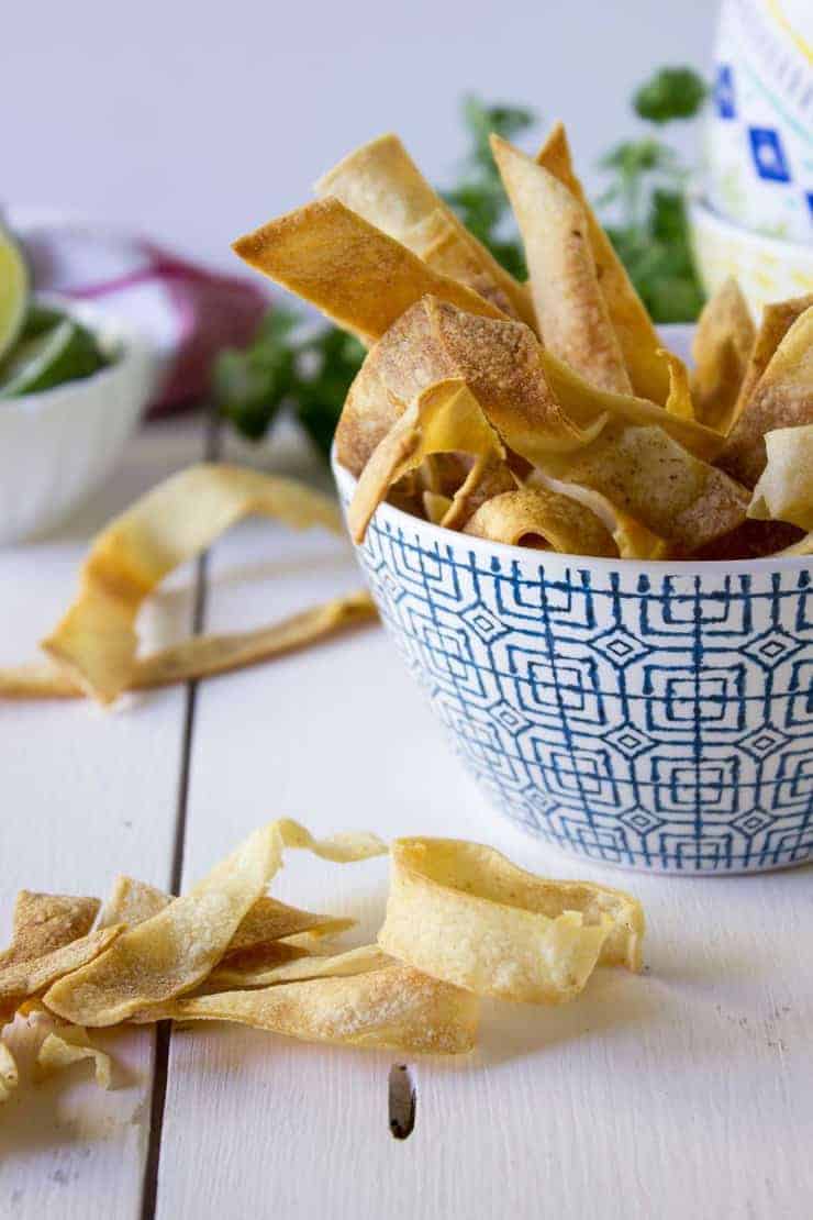 Crispy corn tortillas strips piled on a white board and in a blue patterned bowl. 