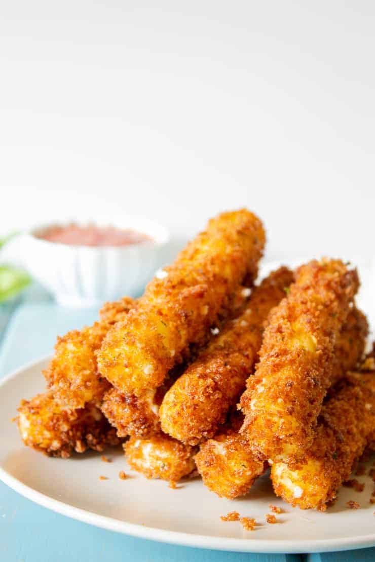 Crunchy coated cheese sticks on a a white plate.