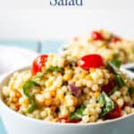 Pasta salad with spinach and tomatoes in a white bowl.