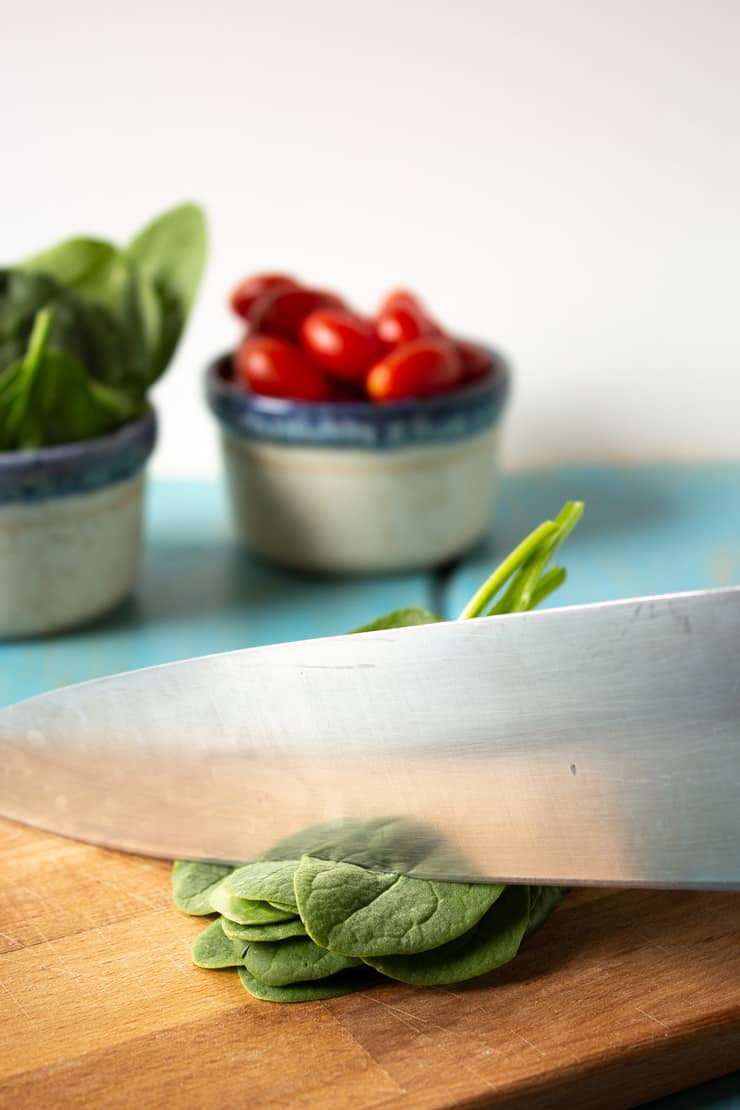 A knife cutting spinach leaves.