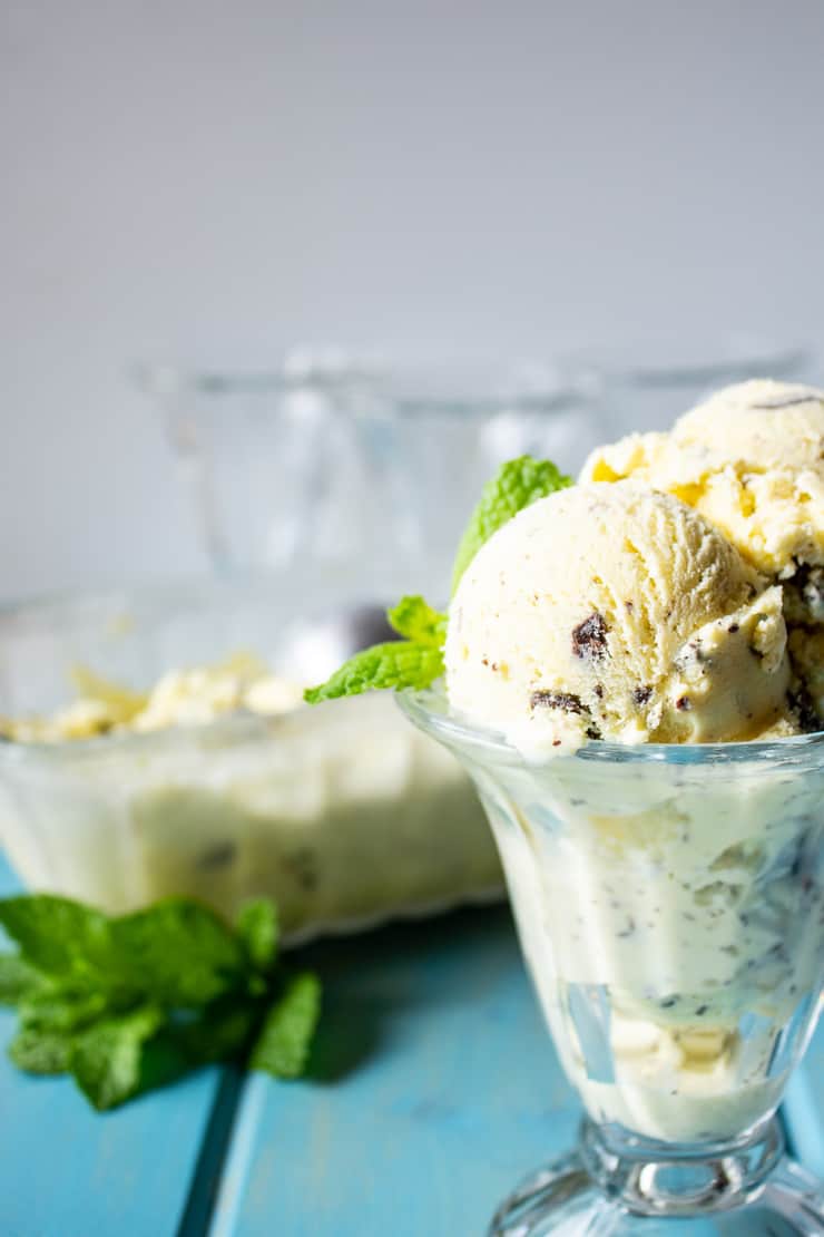 A glass ice cream dish filled with scoops of ice cream with fresh mint garnishing the ice cream.