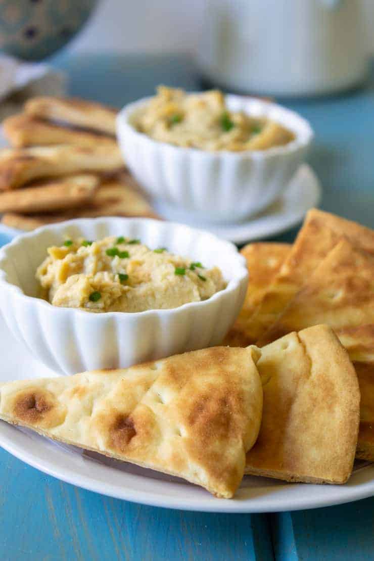 Pita chips on a white plate served with a small bowl of hummus.