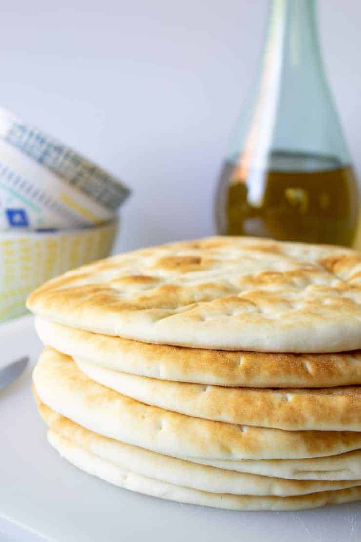 A stack of flat bread and a bottle of olive oil in the background.