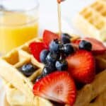 Syrup pouring onto waffles with fresh fruit.