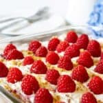 A glass dish filled with whipped cream and topped with fresh raspberries.