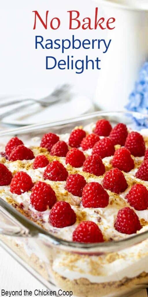 A glass dish filled with whipped cream and topped with fresh raspberries.