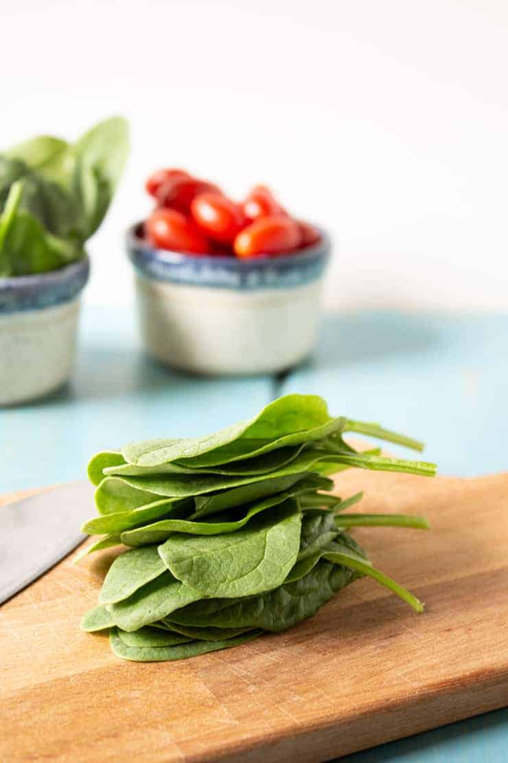 Fresh spinach leaves piled on a cutting board.