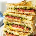 A stacked grilled cheese sandwich with pesto and tomatoes.